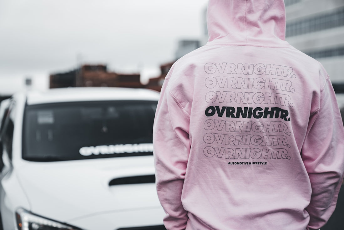 a person in a pink hoodie standing next to a white car