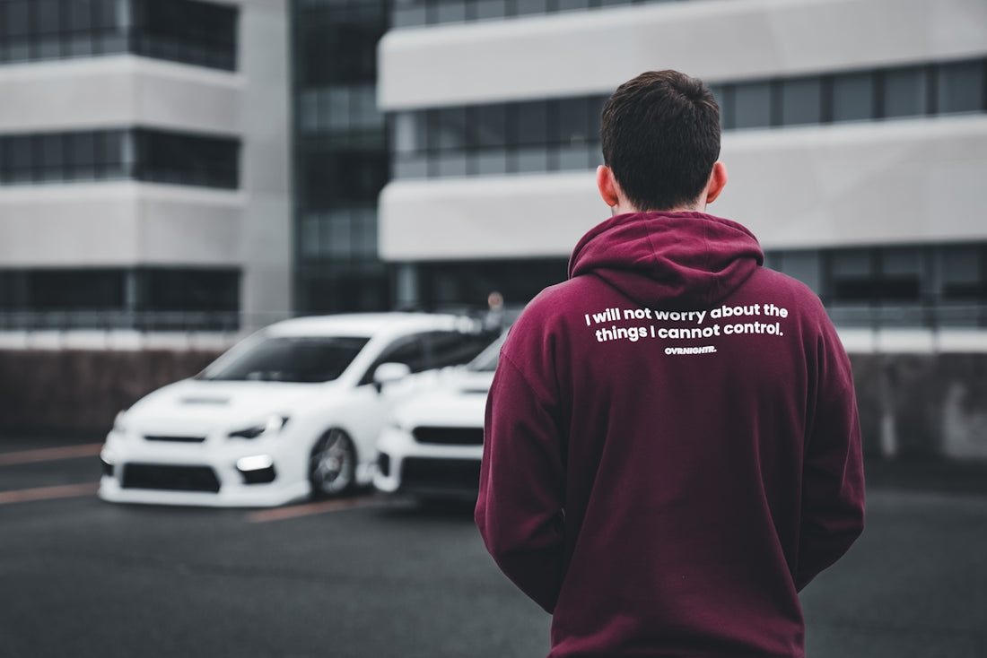 a man in a maroon hoodie standing in front of a white car