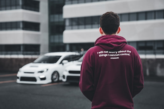 a man in a maroon hoodie standing in front of a white car